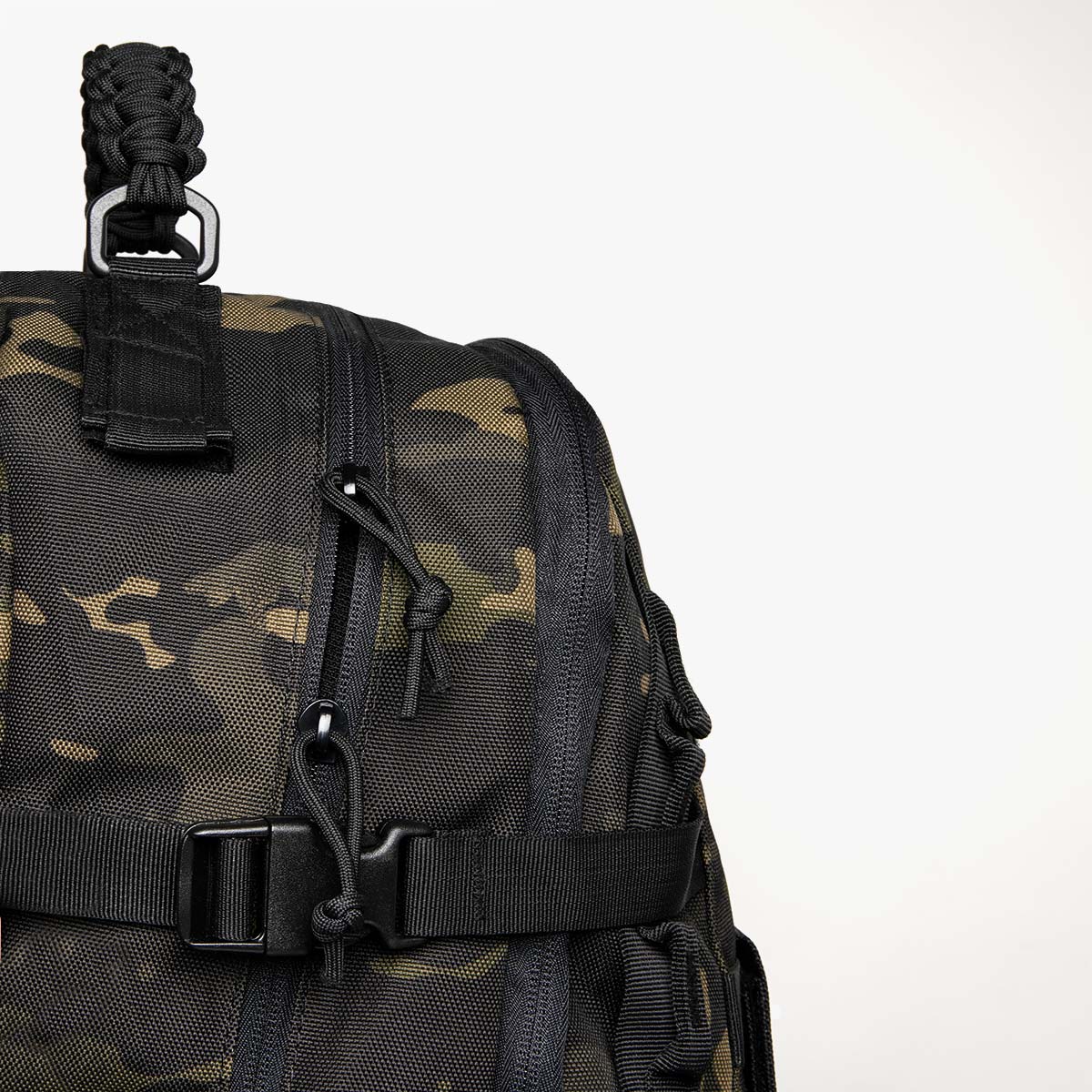 camouflage rucksack Close-up of SAINT tactical backpack showing reinforced carry handle, heavy-duty zippers with paracord pulls, and compression strap