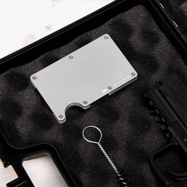 Brushed silver SAINT tactical wallet placed in protective foam case alongside firearm gear