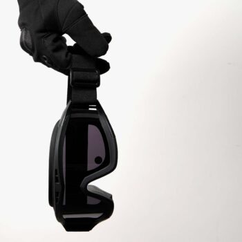 Black SAINT tactical goggles held by strap in a gloved hand