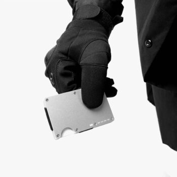 Gloved hand holding a silver SAINT minimalist metal wallet